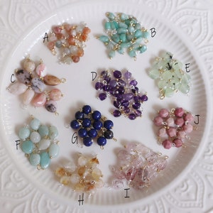 Puede incluir: Diez tipos diferentes de cuentas de piedras preciosas, cada una con un anillo de salto de oro, dispuestas en un plato blanco. Las cuentas están etiquetadas de la A a la J.