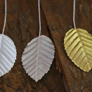 May include: Three artificial leaves with a wire stem. The leaves are made of a shiny material and are white, silver, and gold.