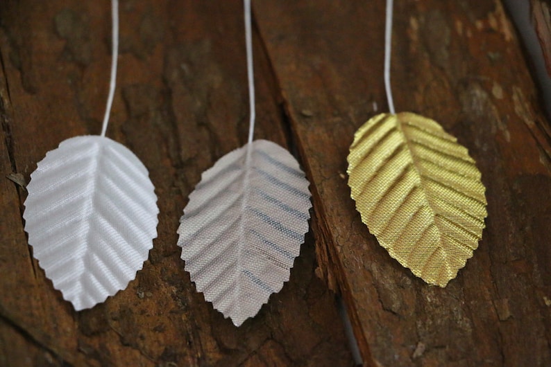 May include: Three artificial leaves with a wire stem. The leaves are made of a shiny material and are white, silver, and gold.