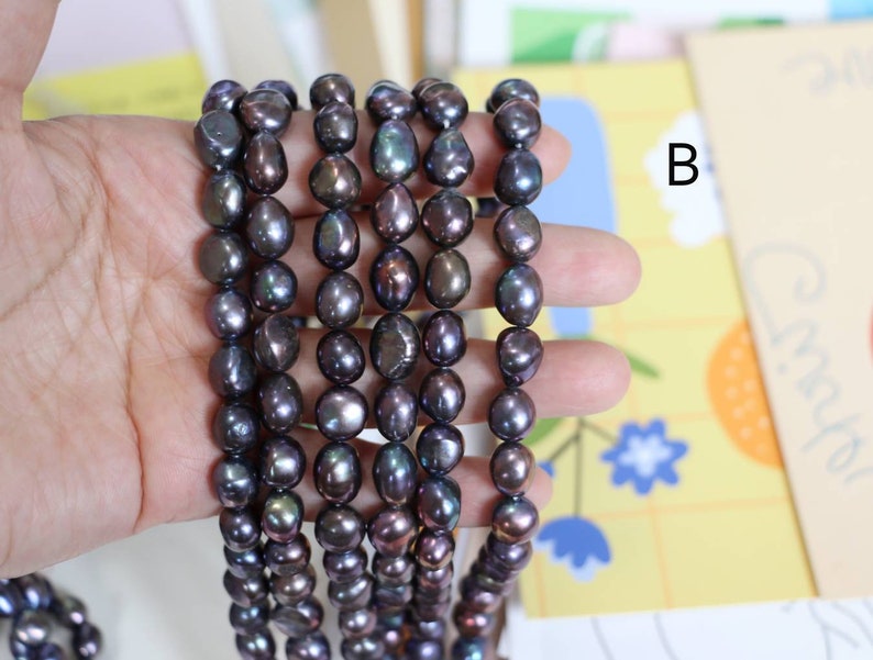 May include: A strand of dark gray baroque pearls with iridescent hues. The pearls are strung on a clear thread and are approximately 8-9mm in size.