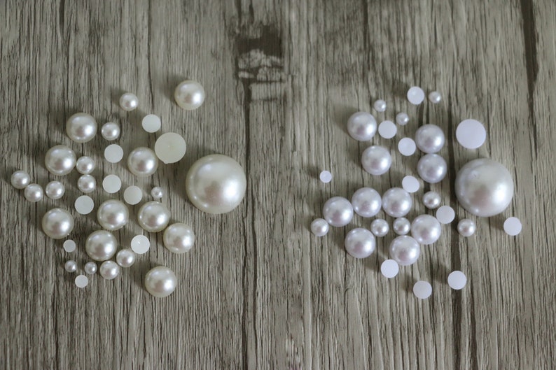 May include: A collection of white pearl beads of various sizes, arranged in two groups on a woodgrain surface.