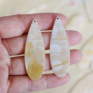 May include: Two white and gold teardrop-shaped resin earrings with a marbled effect.