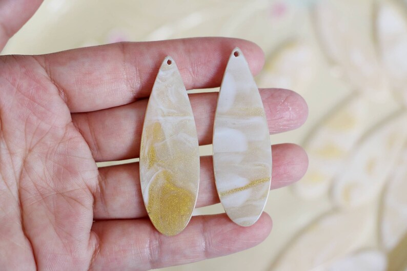 May include: Two white and gold teardrop-shaped resin earrings with a marbled effect.