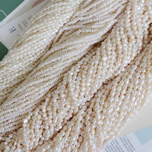 Può includere: Primo piano di più fili di perle d'acqua dolce bianco crema. Le perle variano per dimensioni e forma, creando un aspetto strutturato ed elegante. I fili sono disposti a cascata, suggerendo il loro utilizzo nella creazione di gioielli.