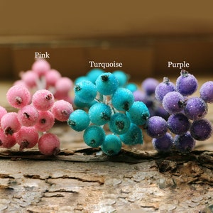 Puede incluir: Tres ramitas de bayas artificiales, cada una de un color diferente: rosa, turquesa y morado. Las bayas est&aacute;n agrupadas y tienen un acabado brillante y escarchado.