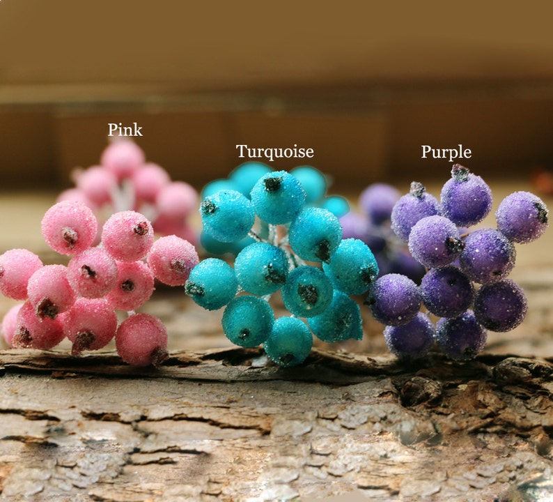 Puede incluir: Tres ramitas de bayas artificiales, cada una de un color diferente: rosa, turquesa y morado. Las bayas est&aacute;n agrupadas y tienen un acabado brillante y escarchado.
