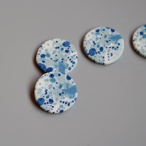 May include: Three round ceramic ornaments with a blue and white speckled pattern. The ornaments have a hole at the top for hanging.