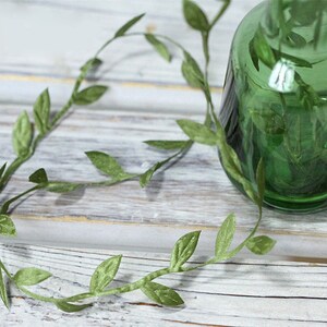 May include: A green glass vase with a decorative vine of green leaves wrapped around it.