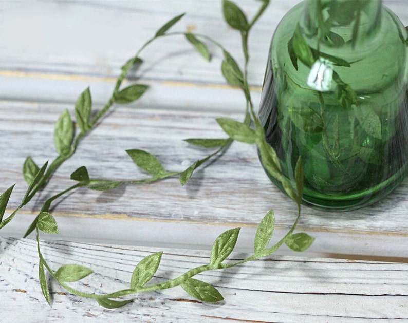 May include: A green glass vase with a decorative vine of green leaves wrapped around it.