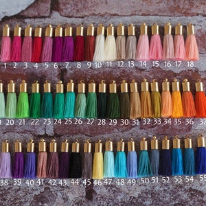 Peut inclure: Une collection de 55 pompons colorés avec des sommets dorés. Les pompons sont disposés en rangées de 18, 19 et 17. Les pompons sont de différentes couleurs, notamment le rouge, le vert, le bleu, le violet et le jaune.