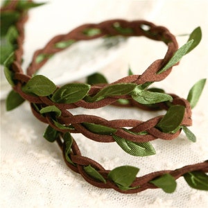 May include: Brown suede cord with green fabric leaves woven into the cord. The cord is braided and has a natural, rustic look.