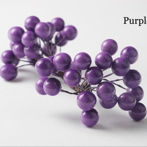 May include: Purple berry sprigs with small round berries. The berries are clustered together on thin wire stems.