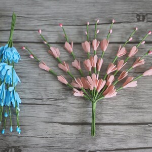 May include: Two bunches of artificial flowers, one blue and one pink, with green stems. The flowers are made of felt and have a delicate, realistic appearance.