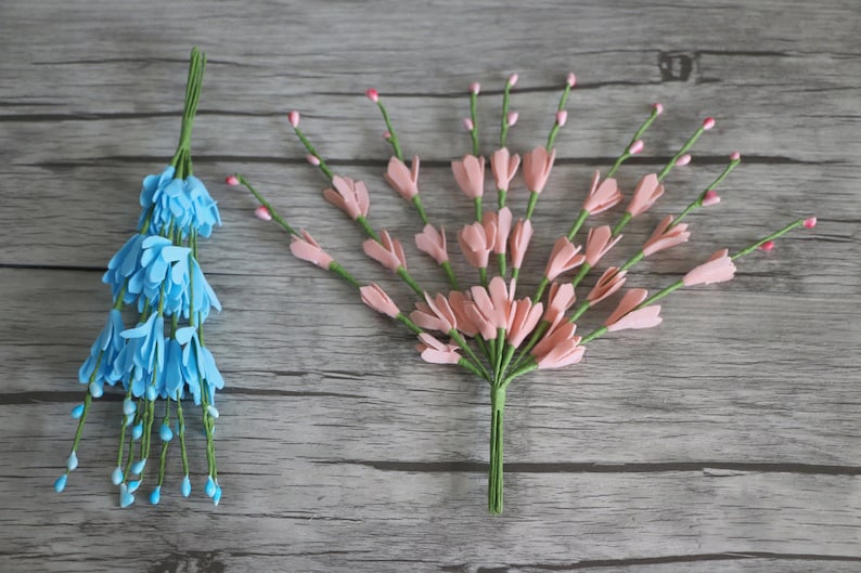 May include: Two bunches of artificial flowers, one blue and one pink, with green stems. The flowers are made of felt and have a delicate, realistic appearance.
