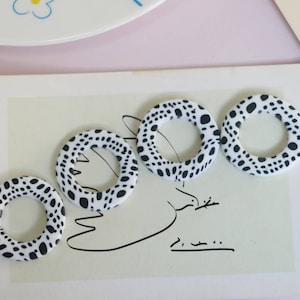 May include: Five white ceramic rings with a black polka dot pattern. The rings are arranged in a row on a white surface.