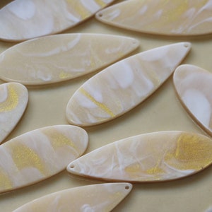 May include: A collection of oval-shaped resin blanks with a marbled pattern in white and gold. The blanks are perfect for crafting earrings, pendants, or other jewelry.