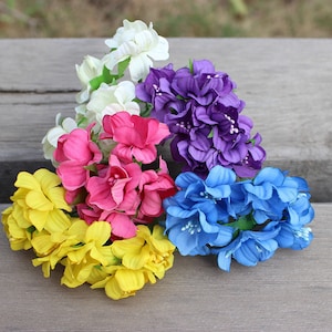 May include: Assortment of six small artificial flower bunches in various colors, including white, purple, pink, blue, and yellow. The flowers are made of fabric and have a realistic appearance.