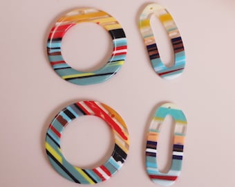 May include: Four colorful acrylic resin shapes with a striped pattern. Two are round with a hole in the center and two are oval with a hole in the center.