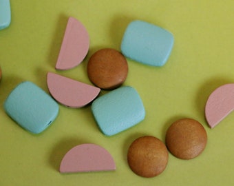 Könnte beinhalten: Eine Sammlung von Holzperlen in verschiedenen Formen und Farben, darunter rosa, blau und braun. Die Perlen sind auf einer grünen Oberfläche angeordnet.