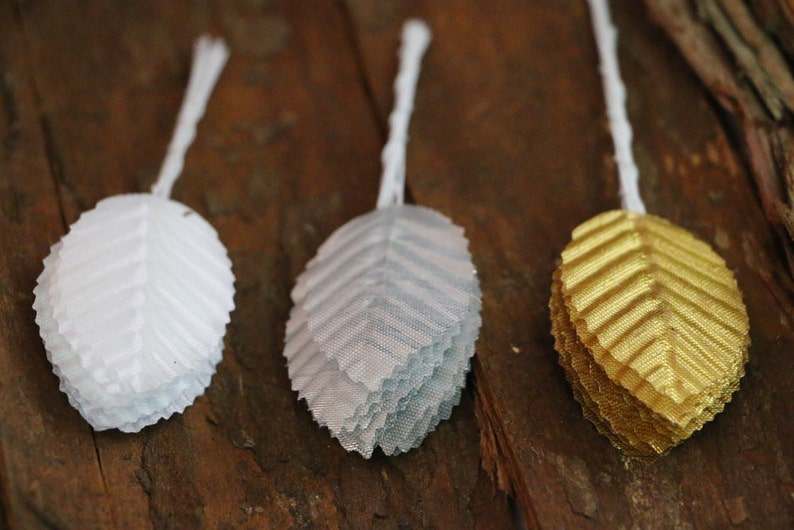 May include: Three fabric leaves in white, silver, and gold. The leaves are layered and have a textured, crinkled appearance.