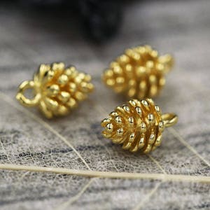 Könnte beinhalten: Drei goldfarbene Metall-Tannenbaum-Anhänger mit einer Öse zum Anbringen an Schmuck oder anderen Bastelarbeiten.
