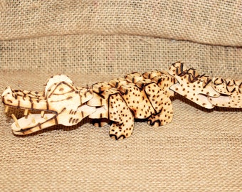 May include: A wooden crocodile toy with a detailed, intricate design. The crocodile is made of light brown wood and has a textured surface. The toy is articulated and can be posed in different positions.