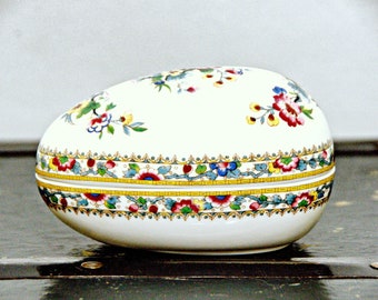 Könnte beinhalten: Eine weiße Porzellan-Schmuckdose in Ei-Form mit einem floralen Design in Blautönen, Rot, Gelb und Grün. Die Dose hat einen goldenen Rand und einen Deckel.
