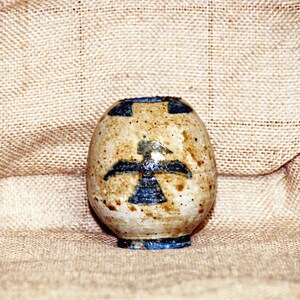 Peut inclure: Un petit vase en céramique blanche avec un motif d'oiseau bleu. Le vase a un glaçage moucheté et une forme arrondie.