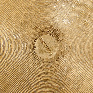 May include: Close-up of a gold-colored metal surface with concentric circles. The center of the surface has a small, circular stamp that reads "Made in U.S.A."