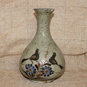 May include: A small, gray ceramic vase with a speckled glaze. It features a hand-painted design of two birds and flowers in shades of blue, brown, and orange.