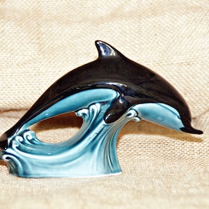 May include: A ceramic dolphin figurine leaping out of the water. The dolphin is black with a blue and white wave base.