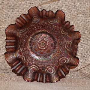 May include: An iridescent, antique-style bowl with a ruffled edge. The bowl has a detailed pattern of floral and geometric designs in shades of brown, copper, and hints of green. The bowl is likely made of glass.