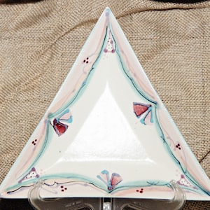 Könnte beinhalten: Eine dreieckige Servierplatte aus Keramik mit weißer Glasur und handbemaltem Design mit rosa, blauen und roten Blumenmotiven.