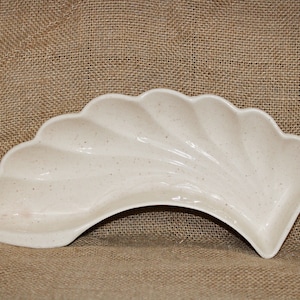 May include: A white ceramic serving dish with a scalloped edge and a speckled finish. The dish is shaped like a crescent moon and is perfect for serving snacks or appetizers.