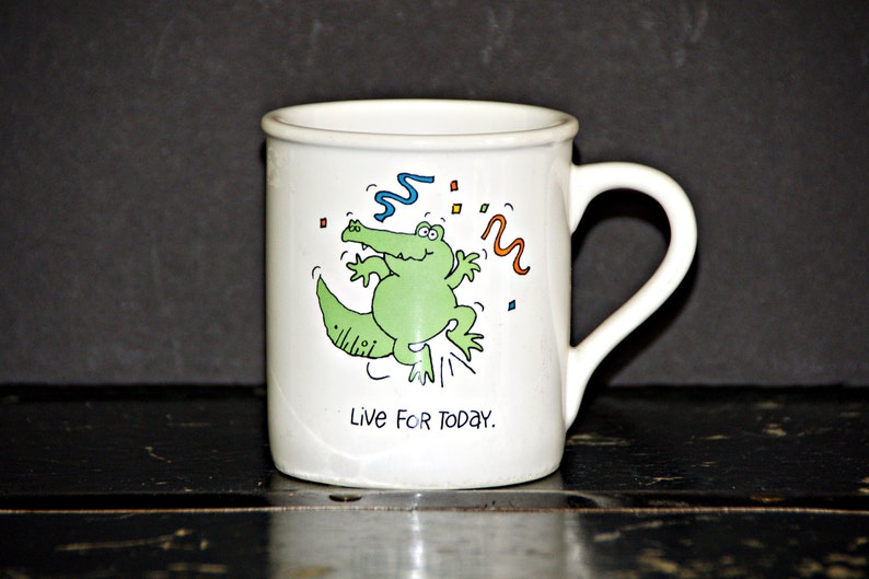 May include: White ceramic mug with a green alligator cartoon illustration and the text "Live For Today."