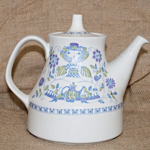 May include: White ceramic teapot with a floral design featuring a girl holding a teacup. The teapot has a spout and a handle. The floral design is in shades of blue, green, and purple.