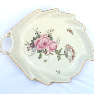 May include: Cream-colored, leaf-shaped serving dish with a gold trim and handle. The dish features a floral design with pink roses, purple flowers, and green leaves. The dish has a textured surface.