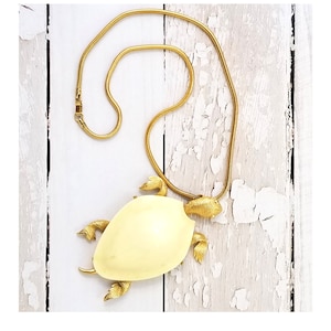 May include: A gold chain necklace with a white turtle pendant. The turtle is detailed with gold accents and has a smooth, white shell.