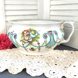 Pode incluir: Um grande vaso de cerâmica branca com uma borda verde e um design floral com flores rosa, amarelas e azuis. O vaso tem um design turquesa e verde com uma alça dourada.