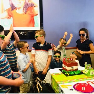 May include: A group of children wearing green and purple glasses celebrate a birthday with a Minecraft-themed cake that says "TNT Ryan".