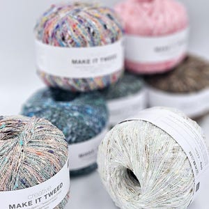 May include: Assortment of colourful yarn balls in various shades of blue, green, pink, and white. The yarn is a tweed blend and is labelled "Make It Tweed" with the text "Tweed-Beaufoam/Tweed A" and "Fil d'accompagnermante" in Italian. The yarn is made in Italy.