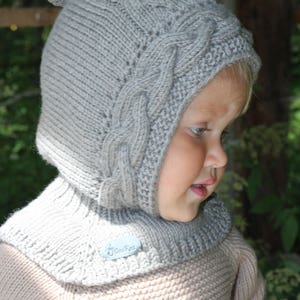 Può includere: Un cappello di lana grigio con un pon pon in cima e un collo a maglia abbinato. Il cappello ha un motivo a treccia e il collo ha un motivo a maglia semplice. Il cappello e il collo sono realizzati in lana morbida e calda.