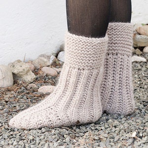 May include: A pair of beige knitted leg warmers with a ribbed texture. The leg warmers are worn over black tights. DROPS DESIGN www.garnstudio.com