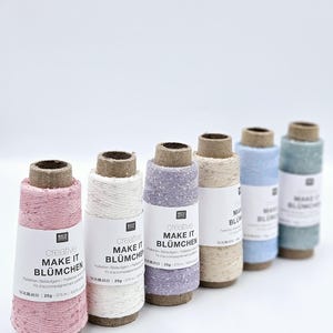 May include: Six spools of creative thread in shades of pink, white, lilac, beige, pale blue, and turquoise. Each spool features a label with the text "MAKE IT BLÜMCHEN". The thread is wound around a cardboard core, with approximately 375 meters of thread.