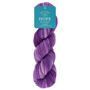 May include: A skein of hand-dyed yarn in shades of purple and white. The yarn is labeled "HOPE" and "Simy's Studio." The yarn is twisted and has a soft, textured appearance. The label is teal with white text.