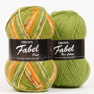 Puede incluir: Dos ovillos de lana, uno verde con estampado multicolor y el otro verde s&oacute;lido. Ambos ovillos tienen la etiqueta "DROPS Fabel" con las palabras "Print" y "Uni Colour" debajo del nombre de la marca.