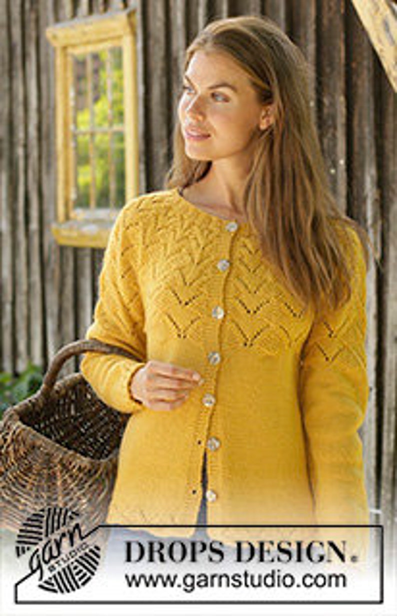 K&ouml;nnte beinhalten: Ein gelber Cardigan mit Knopfleiste und einem zarten Spitzenmuster. Der Cardigan wird von einer Frau mit langen braunen Haaren getragen.