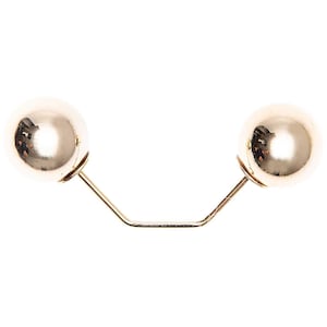 Op de afbeelding: Goudkleurige broche met twee grote, bolvormige ornamenten verbonden door een dunne, gebogen metalen staaf. De bollen hebben een reflecterend oppervlak, tegen een witte achtergrond.