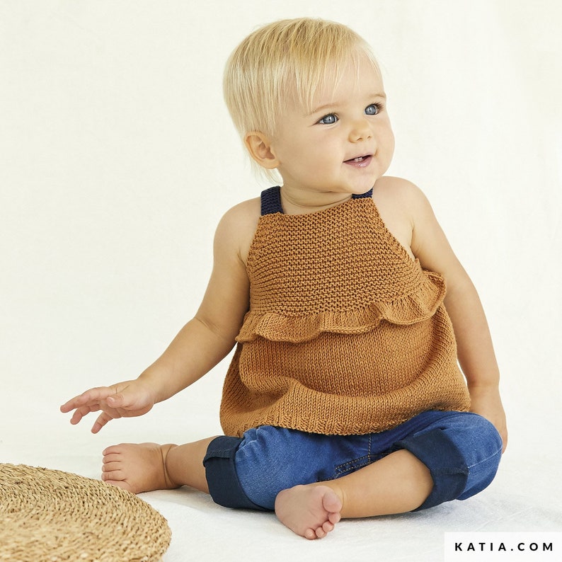 May include: A brown knitted sleeveless top with a ruffled hem and blue straps. The top is worn by a young child with blonde hair.