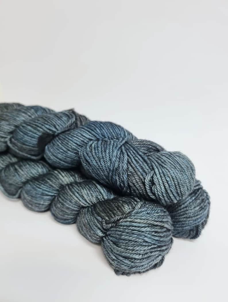 May include: Two skeins of dark blue yarn with a subtle colour variation. The yarn is soft and fluffy, perfect for knitting or crocheting.